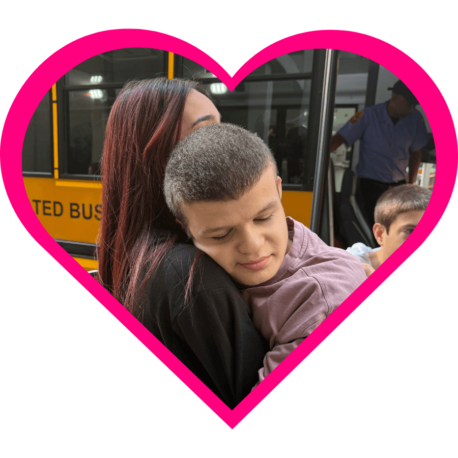 iHOPE student and staff member embrace outside in front of a yellow school bus. 